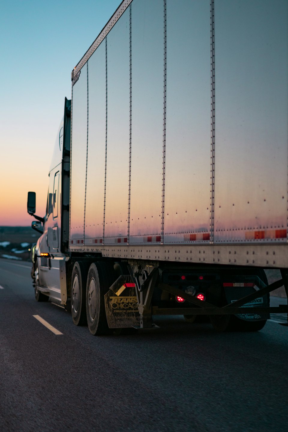 A semi-truck travels down a highway at sunset.