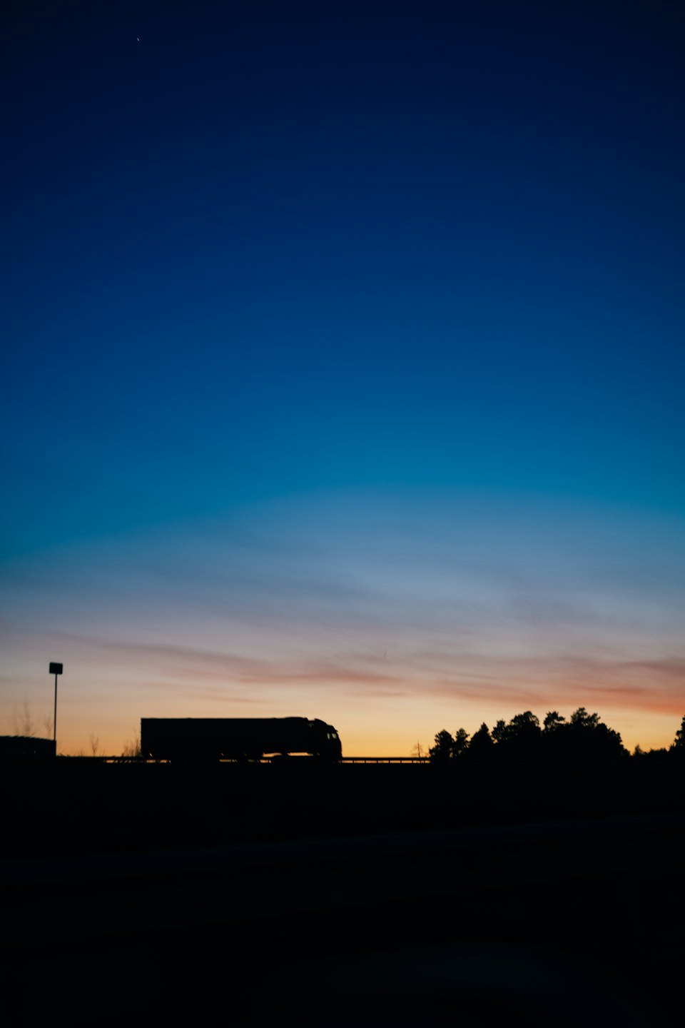 A large semi-truck drives along a highway at sunset.