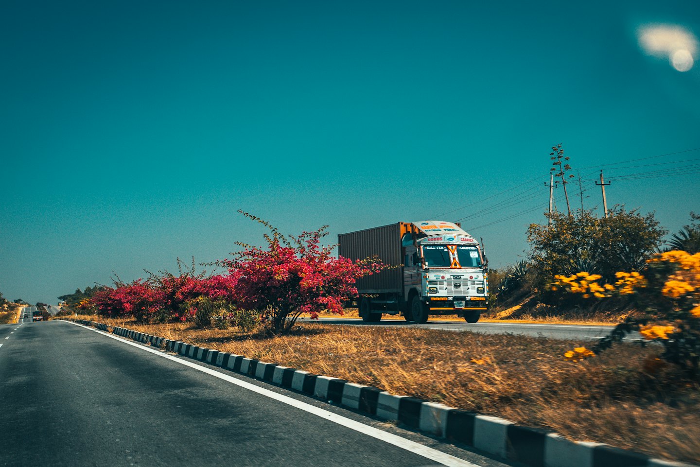 An orange cargo truck drives along a sunny highway.