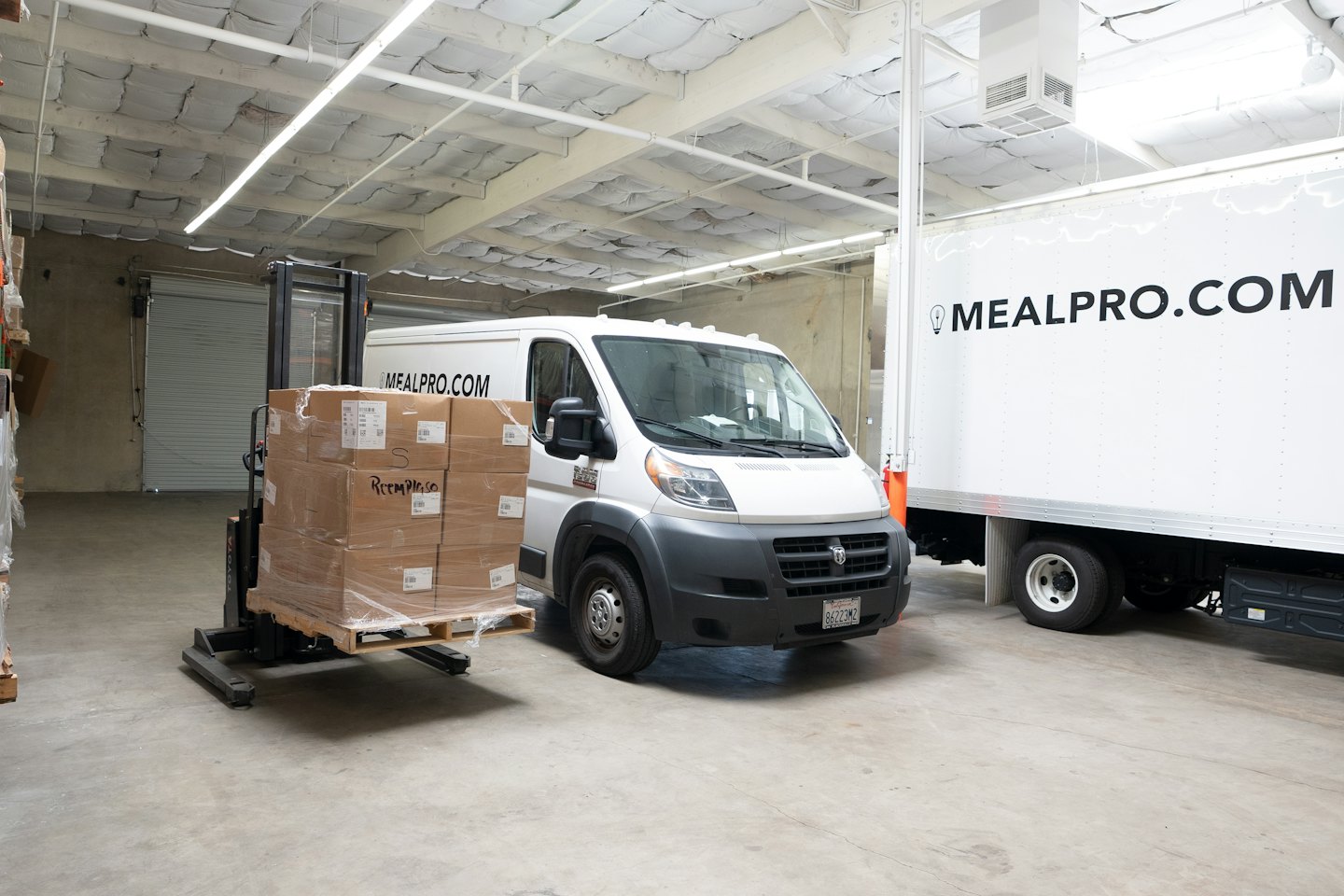 Forklift loads boxes onto a delivery van in a warehouse.