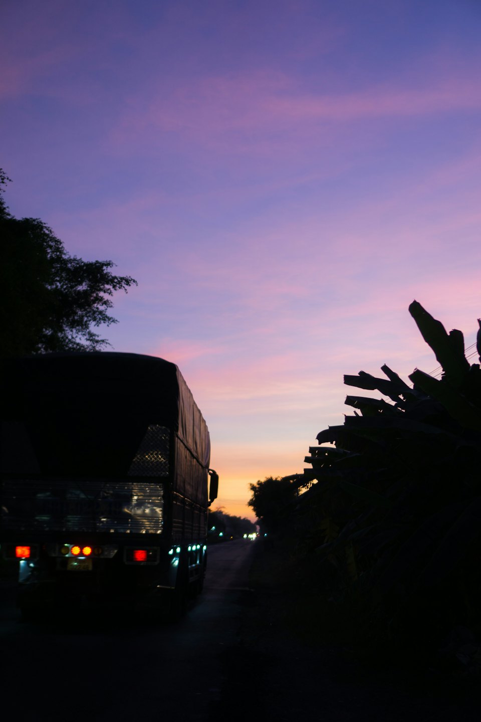 Truck driving on dark road at twilight under colorful sky.